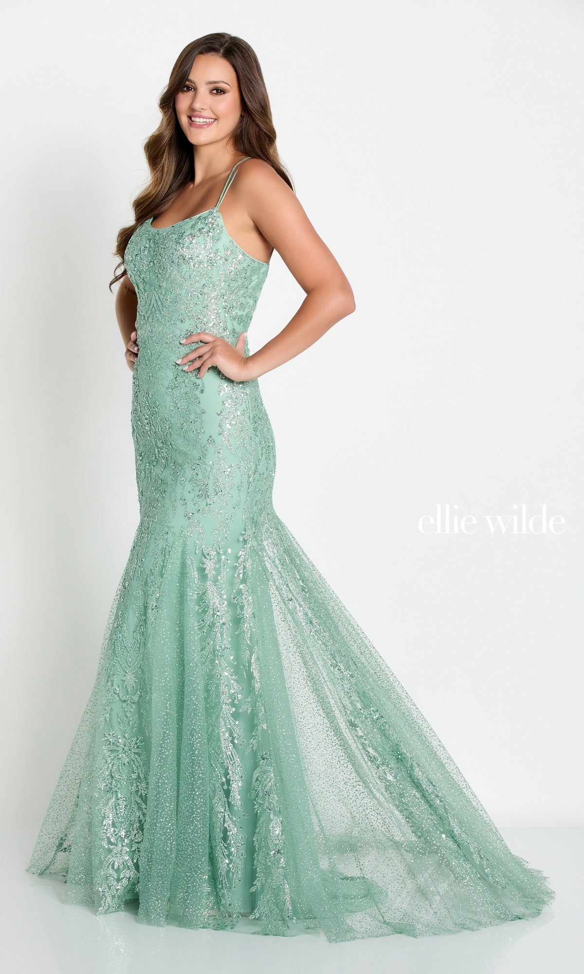 A woman models the Glitter-Jersey Long Mermaid Ellie Wilde Prom Gown—mint green, fitted, with sequin details and spaghetti straps—in a classic mermaid silhouette against a plain white background.
